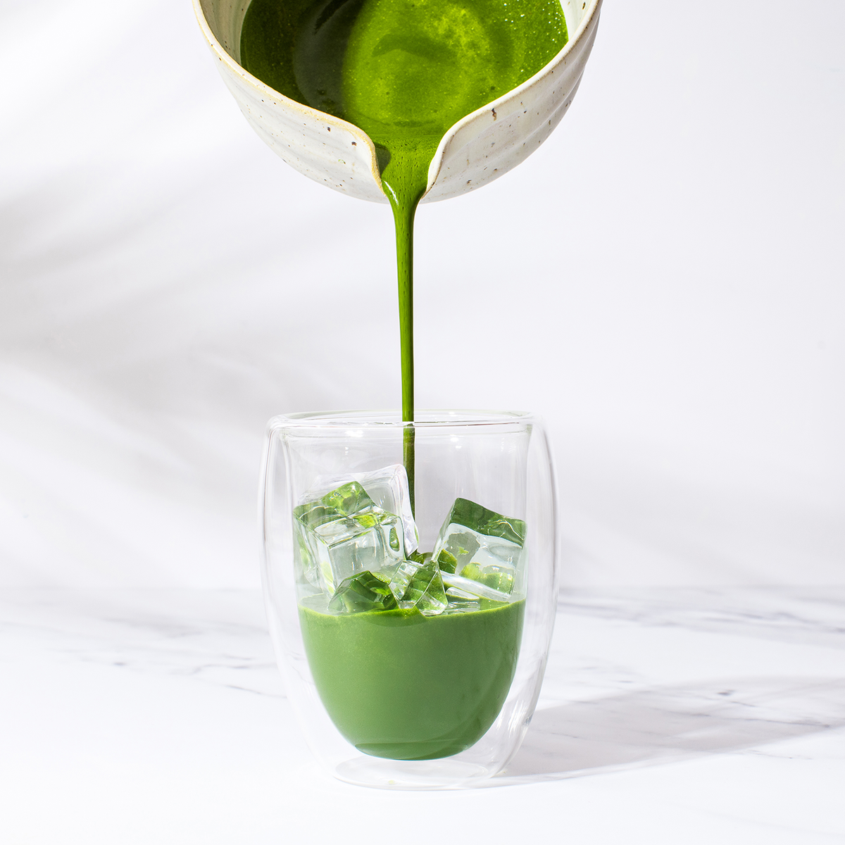 Matcha poured from a ceramic bowl into a glass over ice