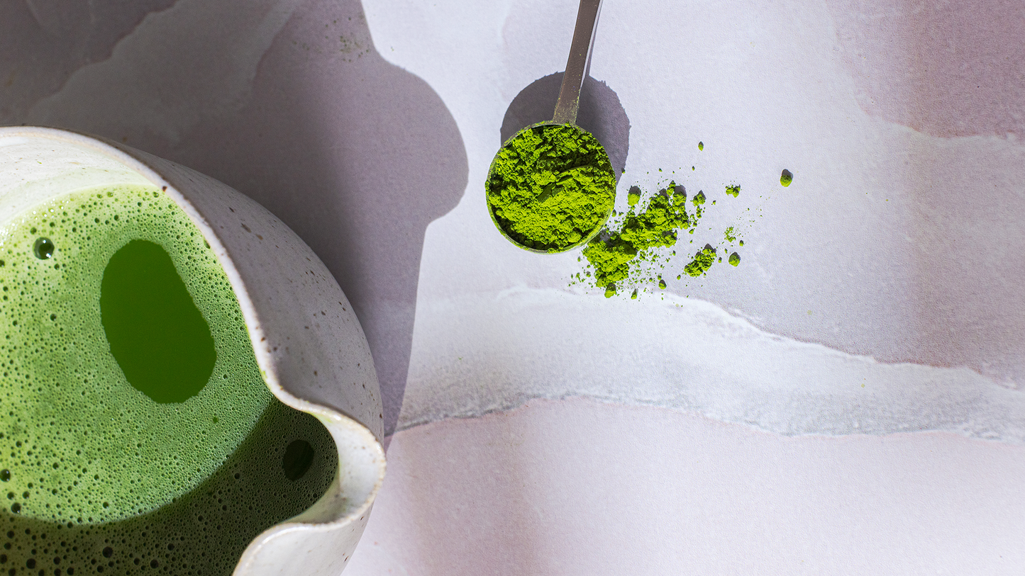 Close up of vibrant green ceremonial matcha powder on a silver Best at Matcha perfect scoop alongside freshly whisked matcha in a ceramic chawan bowl